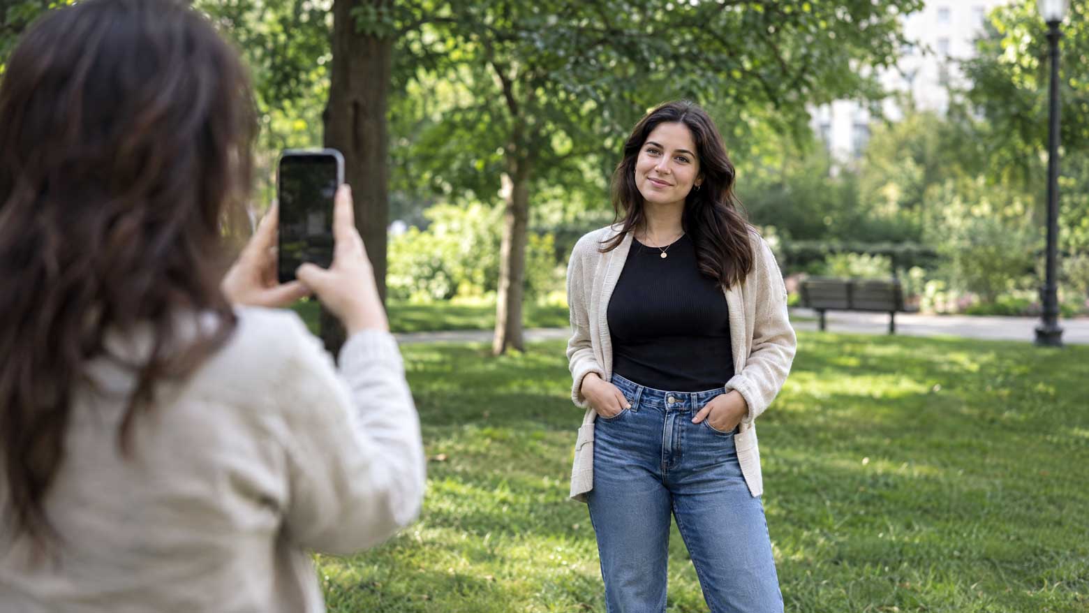 Oseba pozira za portret na prostem v parku z zelenjem v ozadju, medtem ko je fotografirana s pametnim telefonom.
