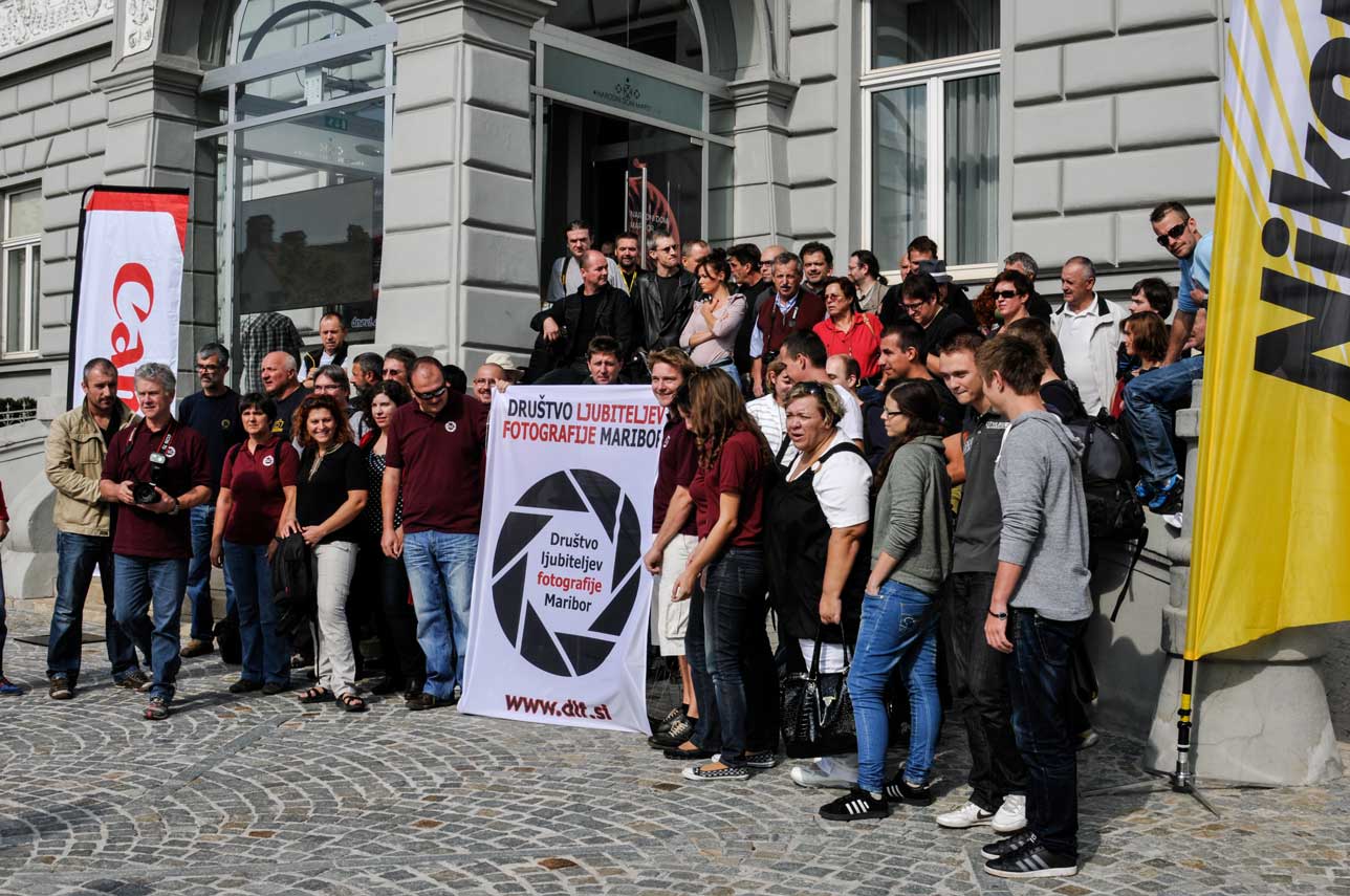 Dnevi fotografije Maribor 2012 Skupina ljudi pred Narodnim domom v Mariboru s transparentom Društva ljubiteljev fotografije Maribor.
